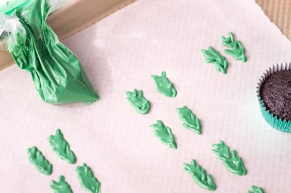 using a piping bag to make holly decorations for cupcakes