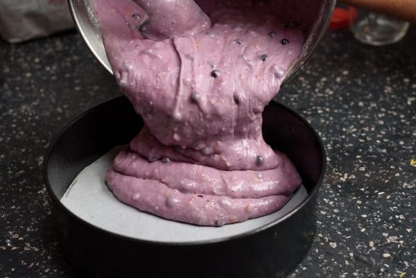 pouring blueberry lemon yogurt cake batter into an 8" cake pan