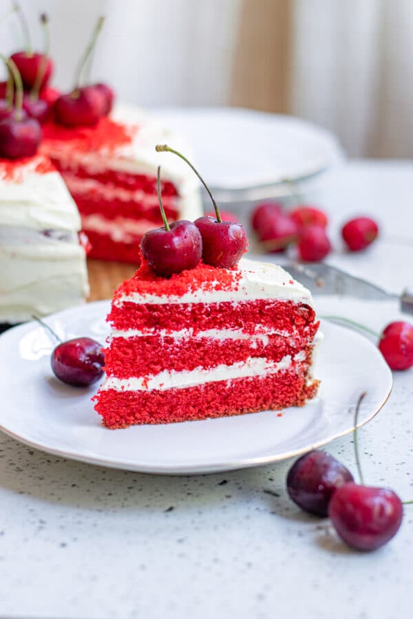 slice of vegan red velvet cake being served, topped with cherries