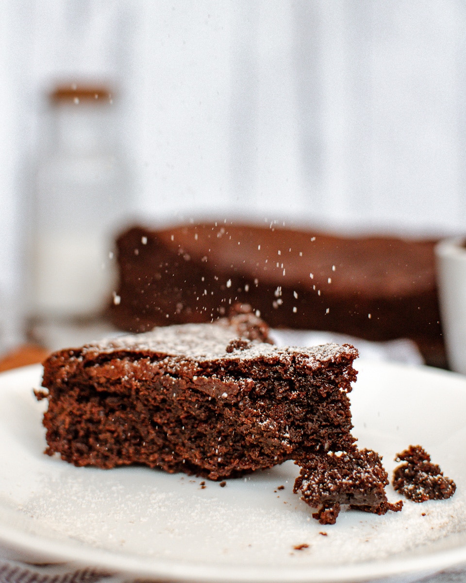 shaking powdered sugar over vegan flourless chocolate cake
