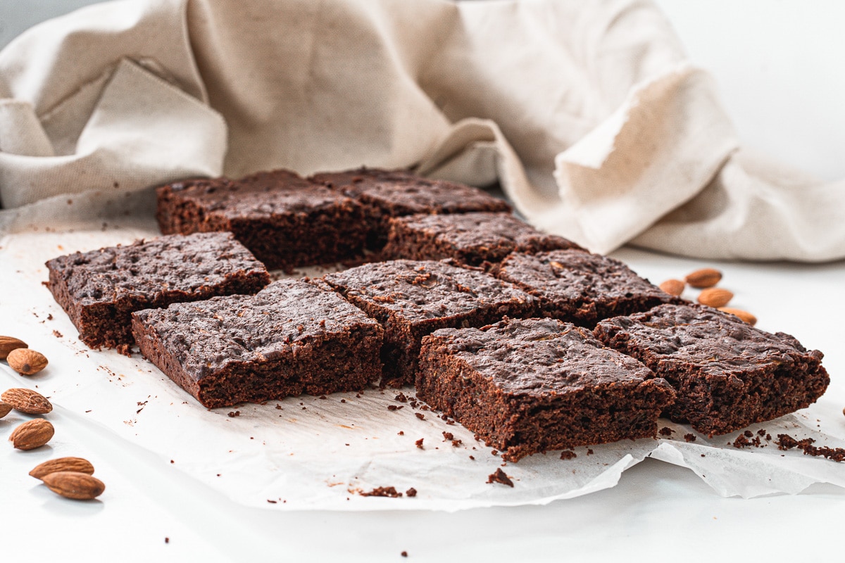 multiple vegan zucchini brownies on a table with almonds