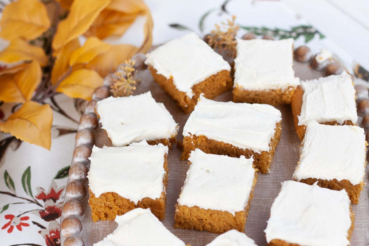 wide view of vegan pumpkin bars on wooden tray with fall leaves