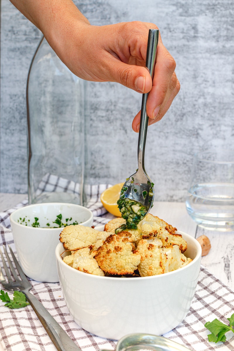wide view of spoon dripping lemon garlic herb sauce over roasted cauliflower